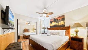 Ein Hotelzimmer mit einem hölzernen Bett, einem Deckenventilator, einem Fernseher und einem Sonnenuntergangsbild.