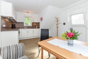 A modern kitchen with white cabinets, a wooden countertop, and a window. There is a dining table with a vase of flowers and a chair.