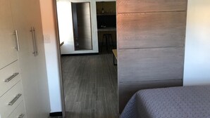 Une chambre moderne avec un lit, une armoire en bois et un coin cuisine à l’arrière-plan.