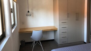 Une chambre à coucher comprenant un lit, un bureau, une chaise, une armoire et un luminaire suspendu.