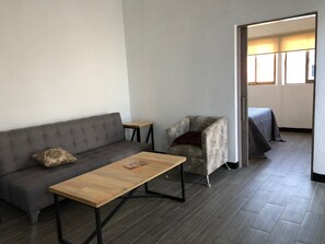 Ein modernes Wohnzimmer mit einem grauen Sofa, einem gemusterten Sessel, einem Holztisch und einem kleinen Beistelltisch.