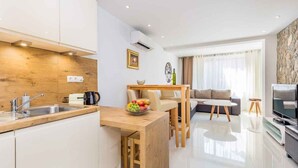 A modern kitchen with a wooden countertop, a dining area with a table and chairs, a living room with a sofa and a TV, and a stone accent wall. - Holiday apartment with modern equipment (Vrbnik)