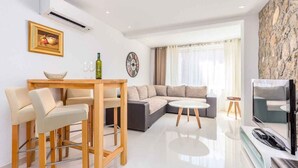 A modern living room with a sofa, a dining table with chairs, a TV, and a stone wall. - Holiday apartment with modern equipment (Vrbnik)