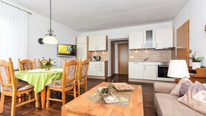 Uma sala de estar moderna com uma mesa de centro de madeira, um sofá e uma área de jantar com cadeiras de madeira e toalha de mesa verde.