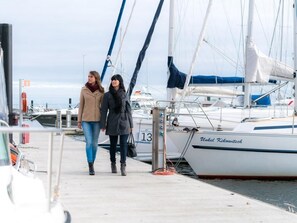 Two people walking along a dock with boats moored nearby.