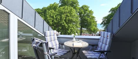 An outdoor seating area with striped chairs and a round table, overlooking a body of water and trees.