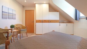 A bedroom with a bed, a seating area with chairs, a small table, and a kitchenette.
