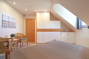 A bedroom with a bed, a seating area with chairs, a small table, and a kitchenette. - Villa Seegarten Whg. Seg11 (Ostseebad Boltenhagen)