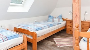 A dormitory room with two wooden beds, a skylight, a wooden wardrobe, and a nightstand.
