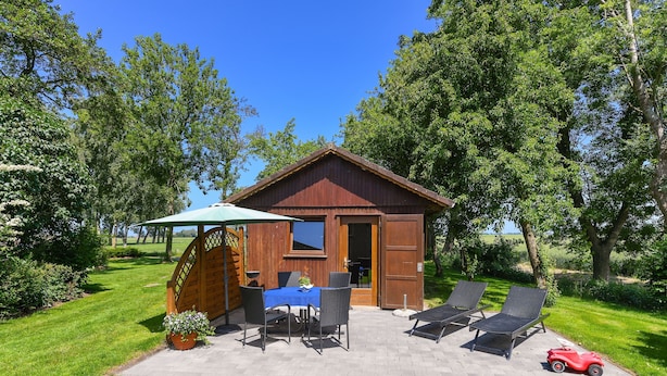 A wooden cabin with a patio, two lounge chairs, a table with chairs, and a small red toy car.