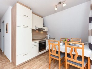 A compact kitchen with white cabinets, a wooden countertop, and a dining area with a table and chairs.