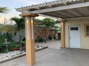 Um espaço coberto ao ar livre com piso de concreto, palmeiras e plantas em vasos.