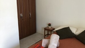 Une chambre à coucher avec un lit, des oreillers, une petite table sur laquelle se trouve un vase, et une armoire.