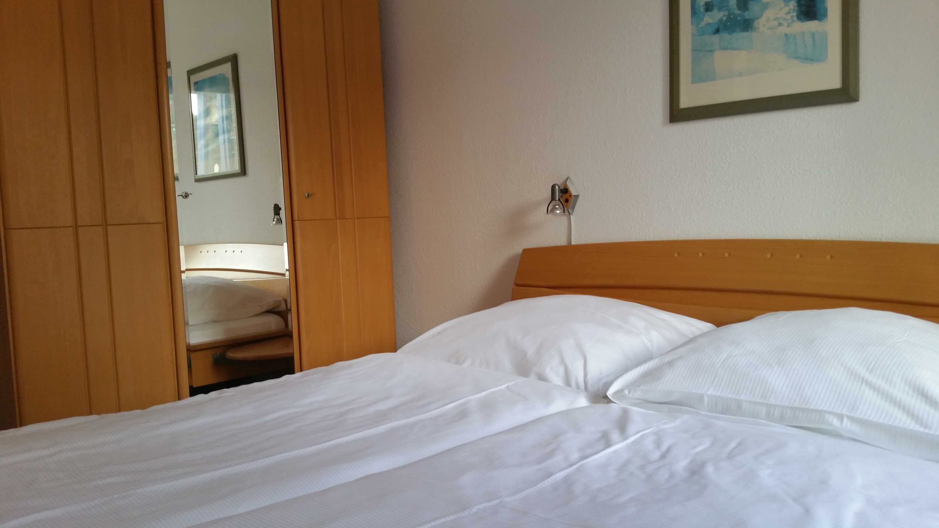 Ein Hotelzimmer mit Bett, Holzschrank und einem gerahmten Bild an der Wand.