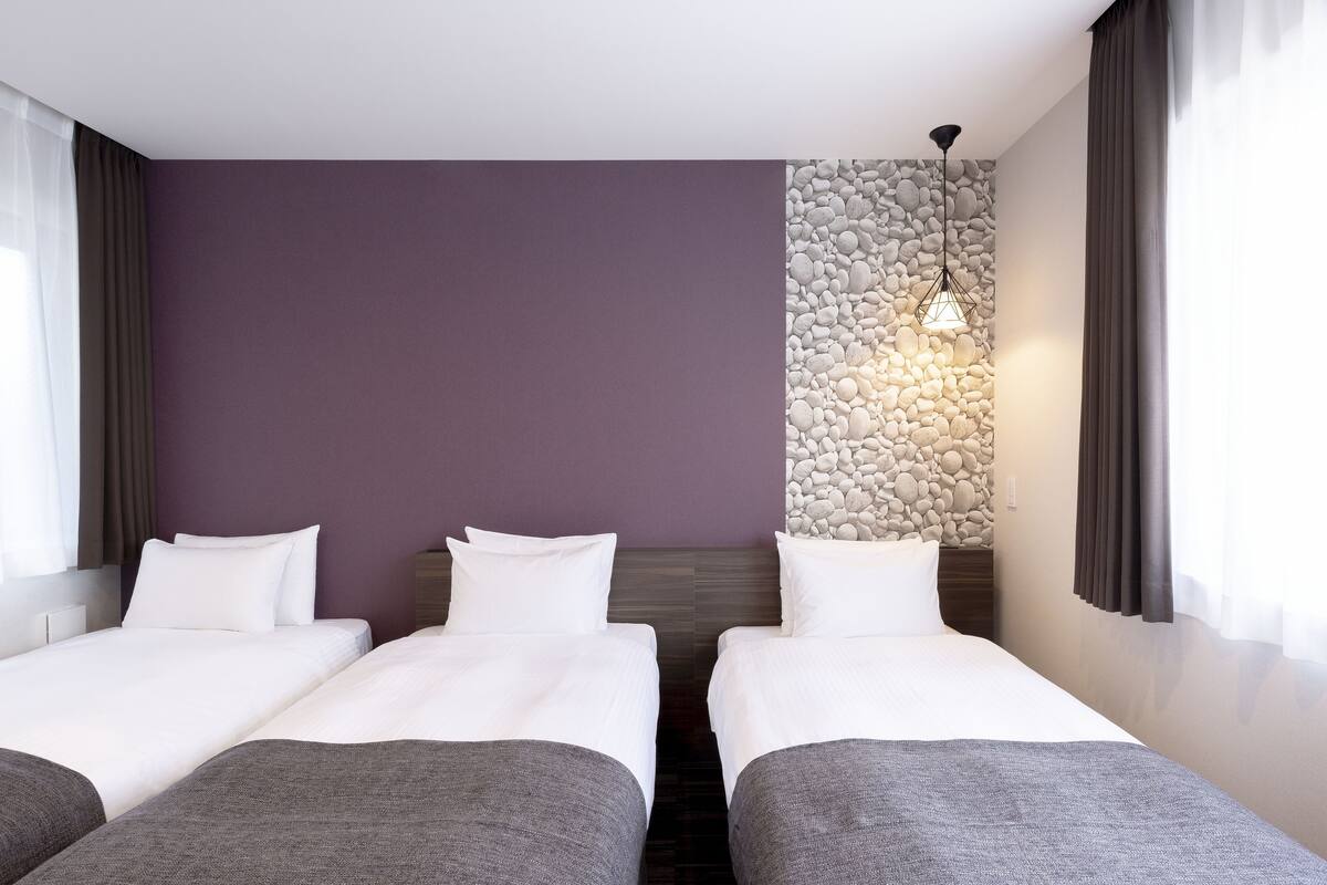 Ein Hotelzimmer mit zwei Betten, einer Steinsäule und einer modernen Lampe.