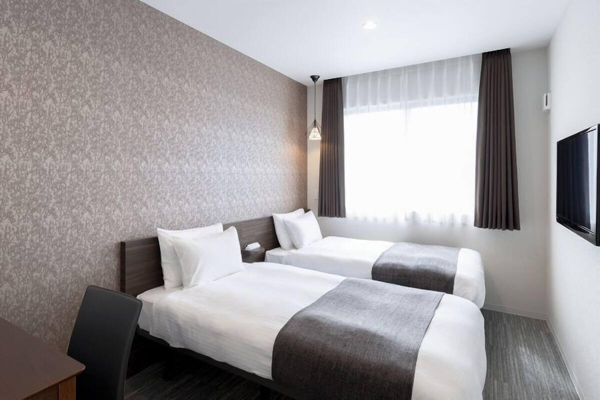 Ein Hotelzimmer mit zwei Betten, einem Schreibtisch, einem Fernseher und einem fenster mit Vorhängen.