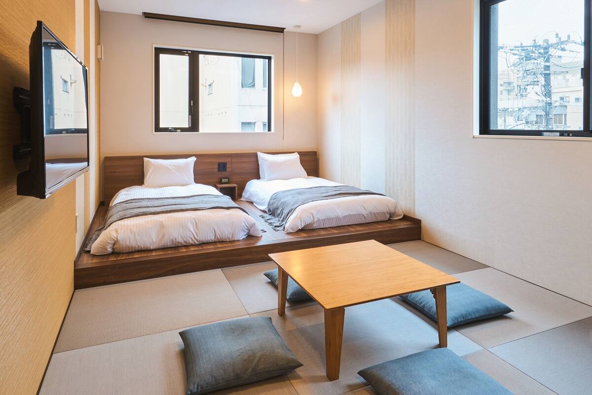 Ein modernes Hotelzimmer mit zwei Betten, einem Holztisch und Tatami-Matten auf dem Boden.