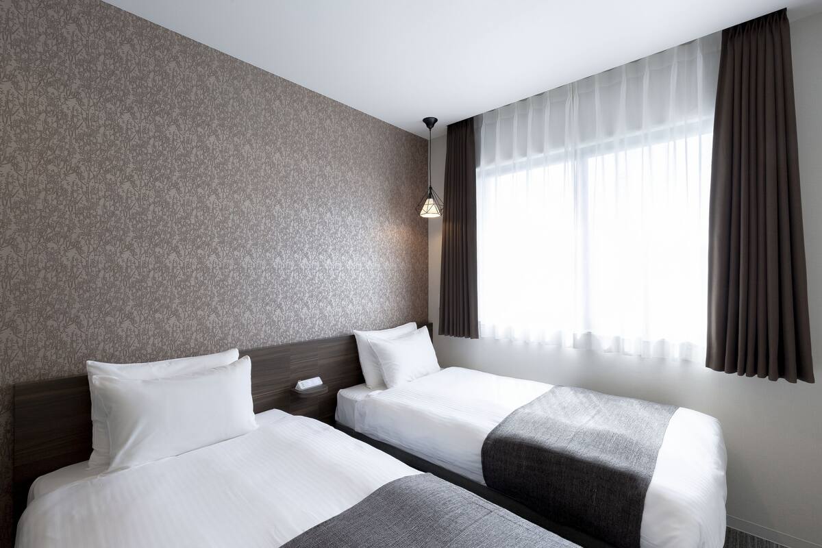 Ein Hotelzimmer mit zwei Betten, einer Wand mit Muster, einem Fenster mit Vorhängen und einer Hängelampe.