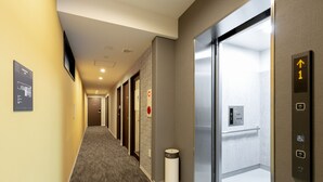 A hotel corridor with an elevator, a trash bin, and a sign indicating the direction to the elevator. - M’s Hotel Gojo Naginatagiri (Kyoto)