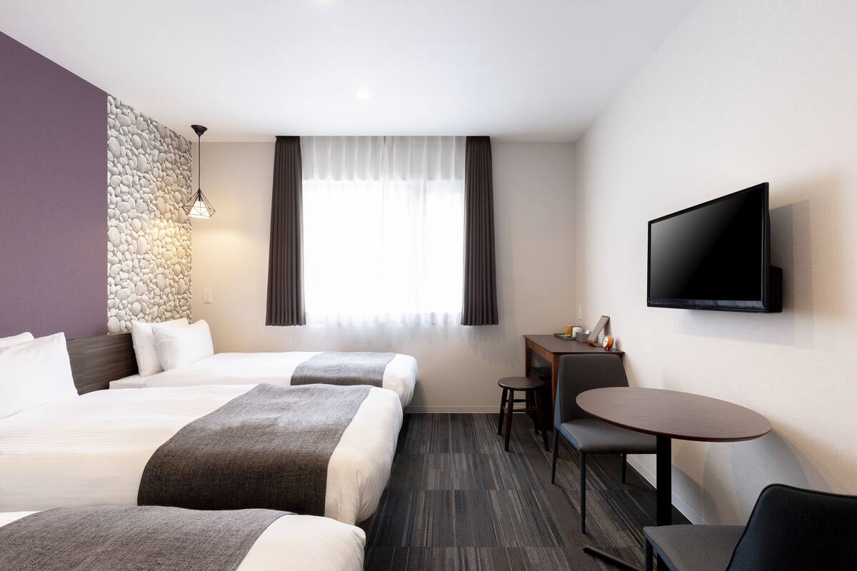 Ein Hotelzimmer mit zwei Betten, einem Schreibtisch, einem Stuhl, einem Fernseher und einer Steinwand.