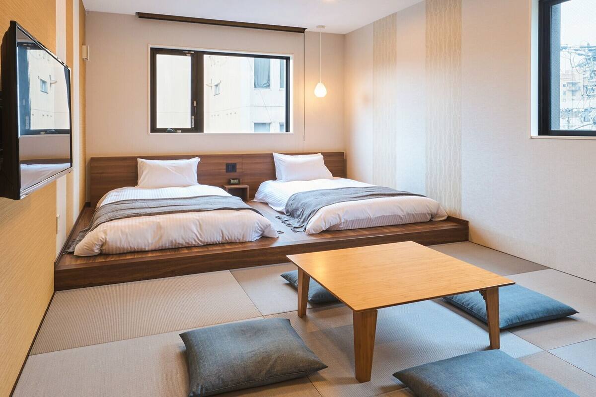 Ein Zimmer mit zwei Betten, einem Holztisch und Tatami-Matten.