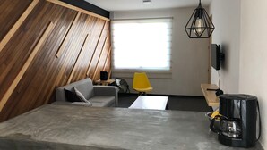 Un saló modern amb un sofà, una cadira groga, una cafetera i una televisió penjada a la paret.