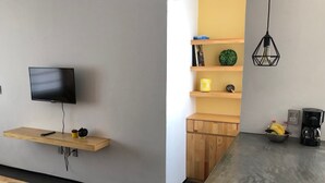 Una cuina moderna amb televisió integrada, prestatges de fusta, una cafetera i un bol de fruita.