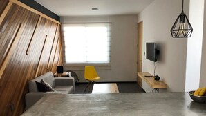 Un espai modern d'estar amb una paret decorativa de fusta, un sofà gris, una cadira groga, una taula de menjador i un televisor muntat a la paret.