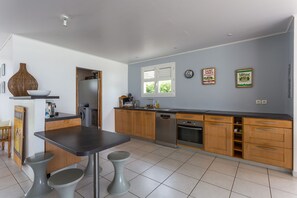A modern kitchen with a dining area, featuring a built-in oven, dishwasher, and a window with blinds.