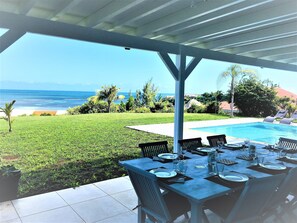 A covered outdoor dining area with a view of the ocean and a swimming pool.