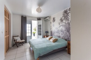 A bedroom with a bed, a chair, a door, and a wall with a tropical mural.