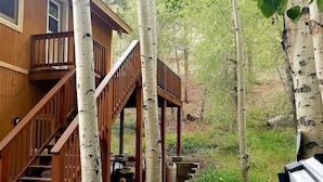 Un bain à remous doté d’une terrasse en bois et d’un escalier menant à une maison en bois, elle-même entourée de bouleaux.