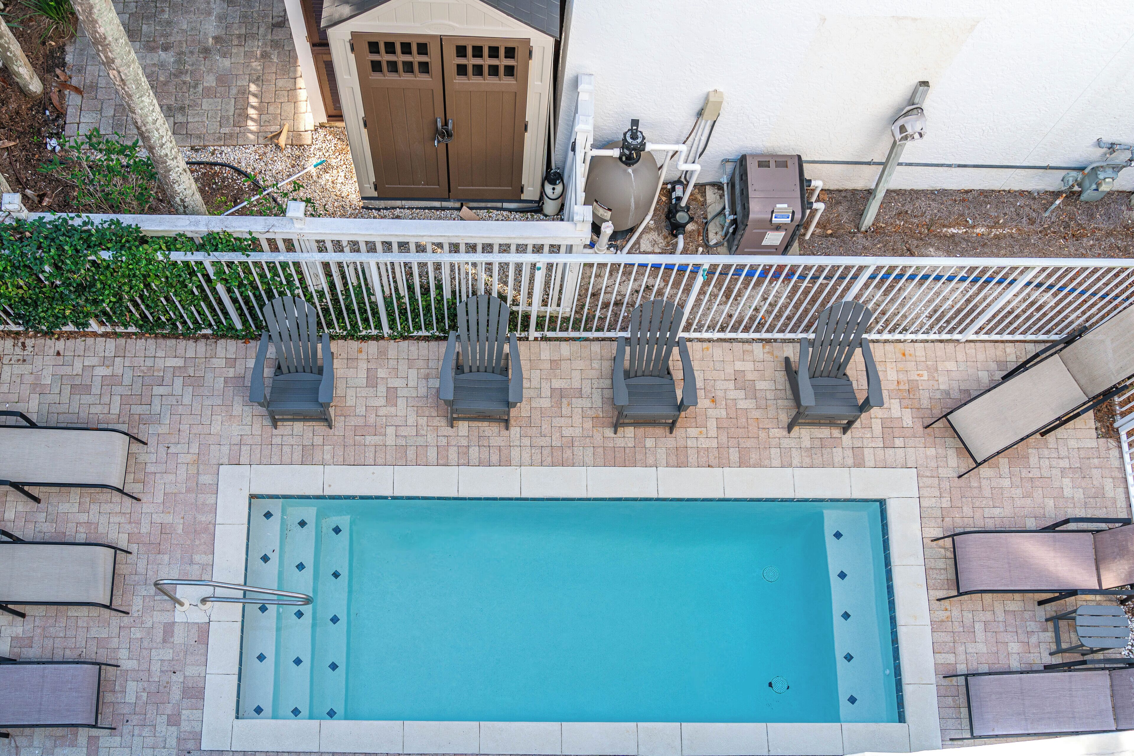 An outdoor swimming pool with a white fence, lounge chairs, and a door in the background.