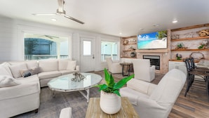 A modern living room with a sectional sofa, a glass coffee table, and a TV mounted on a wooden wall. - Seagrove, Amazing Gulf Views, Great Beach Access, Heated Pool, Pup Friendly
 (Santa Rosa Beach)