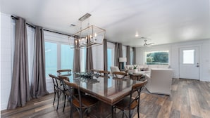 A spacious dining area with a large wooden table and chairs, a modern chandelier, and large windows with curtains. - Seagrove, Amazing Gulf Views, Great Beach Access, Heated Pool, Pup Friendly
 (Santa Rosa Beach)