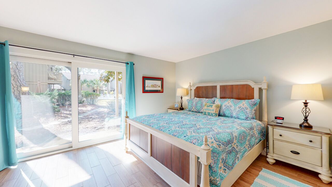 A bedroom with a bed, a nightstand, a lamp, and a sliding glass door leading to an outdoor area.