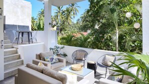 A modern outdoor living area with a sofa, chairs, and a dining table, surrounded by lush greenery and palm trees. - Villa Dorado - Villas del Palmar (Sayulita)