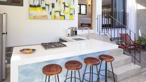 A modern kitchen with a central island, bar stools, and a painting on the wall. - Villa Dorado - Villas del Palmar (Sayulita)