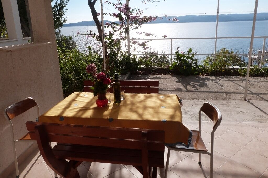 A patio with a table and chairs, a vase with flowers, and a view of a body of water.