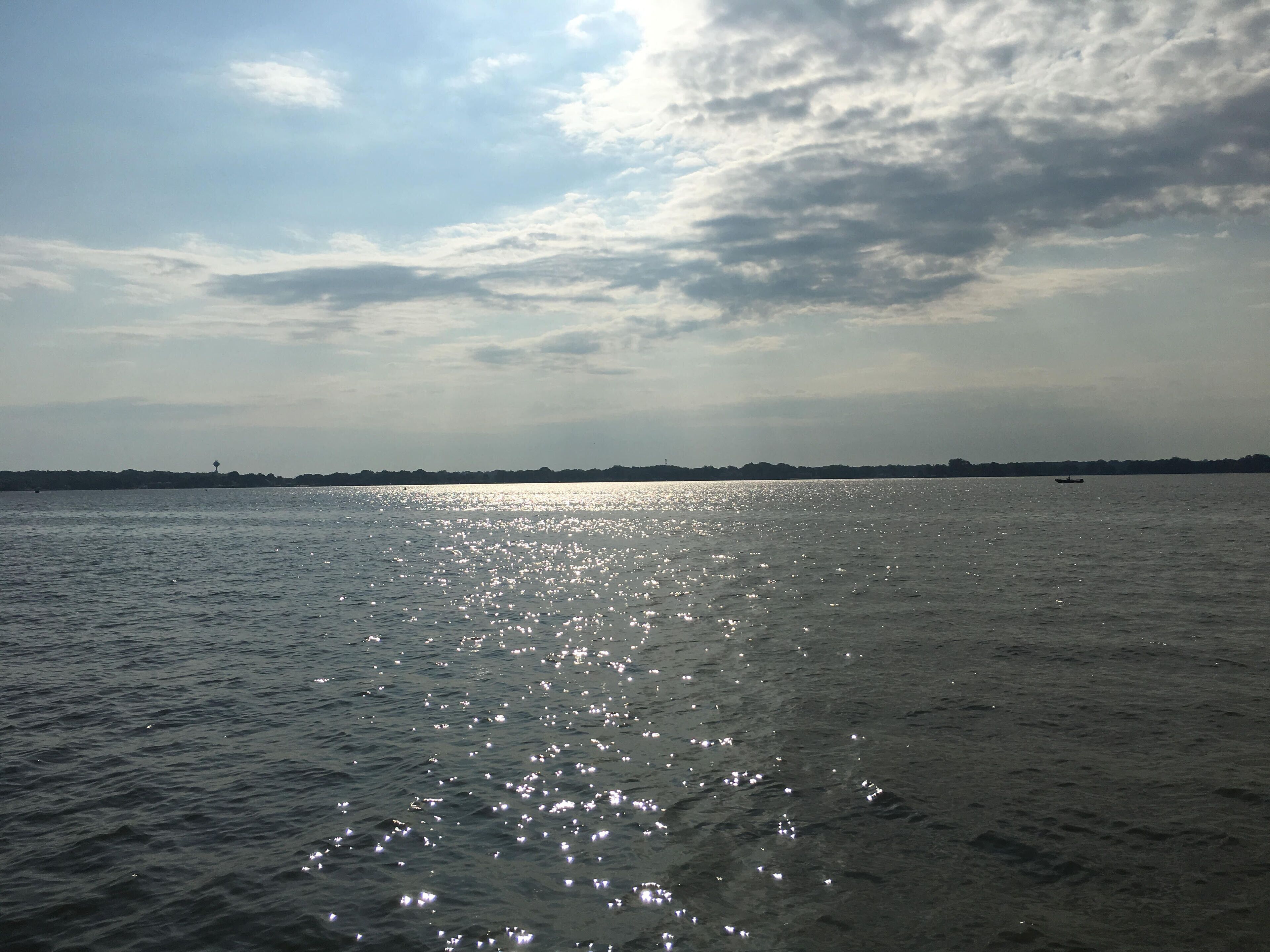 A calm body of water reflecting sunlight with a distant shoreline and a small boat.