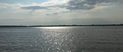A calm body of water reflecting sunlight with a distant shoreline and a small boat.