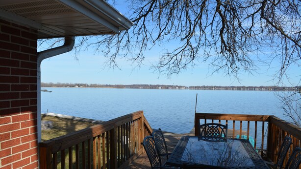 A wooden deck with a table and chairs overlooking a calm body of water.