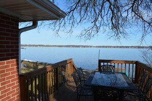 A wooden deck with a table and chairs overlooking a calm body of water. - Lakefront, Newly Renovated, Tranquil Getaway, Free Water Sports (McHenry)
