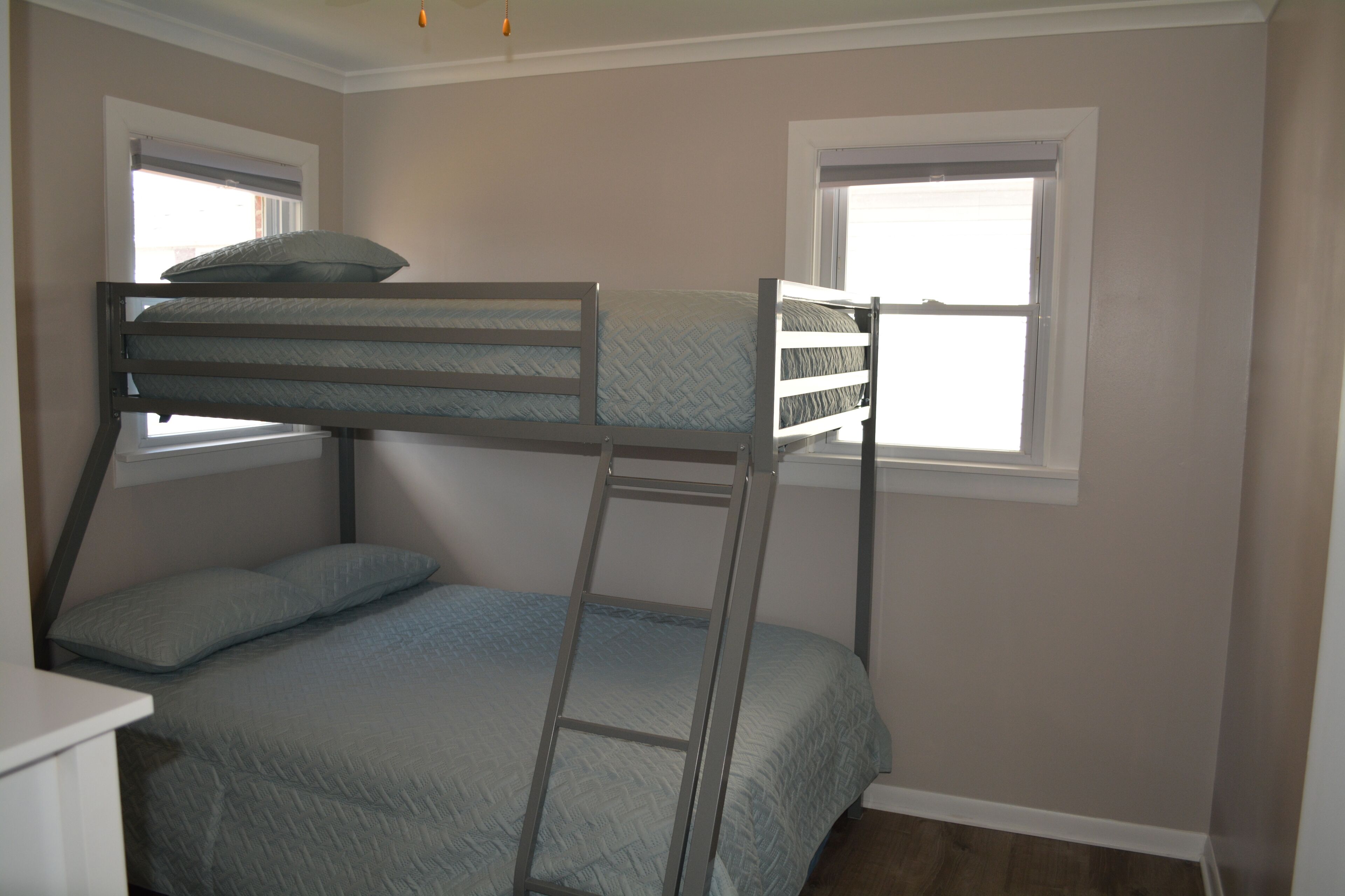 A bunk bed room with a ladder, two windows, and a white dresser.