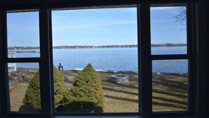 A view through a window of a lake with two coniferous trees and a stone structure on the shore.