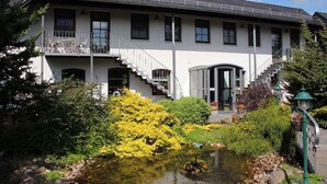 A two-story building with a balcony, a pond, and a garden with yellow flowers.