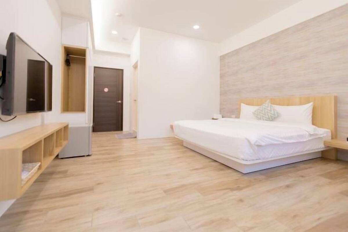 Un dormitorio moderno con una cama, un televisor, un armario y suelo de madera.