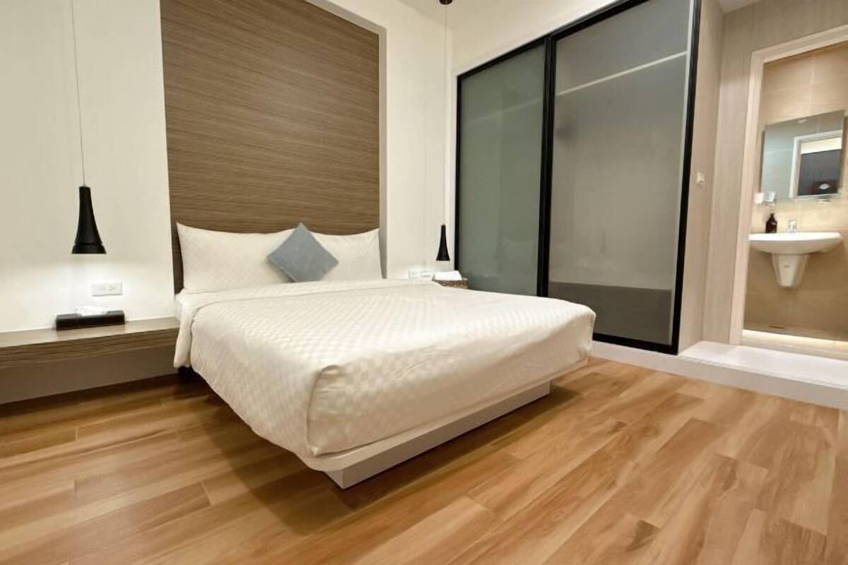 Un dormitorio moderno con cama, mesitas de noche, un tocador y un baño con lavamanos.