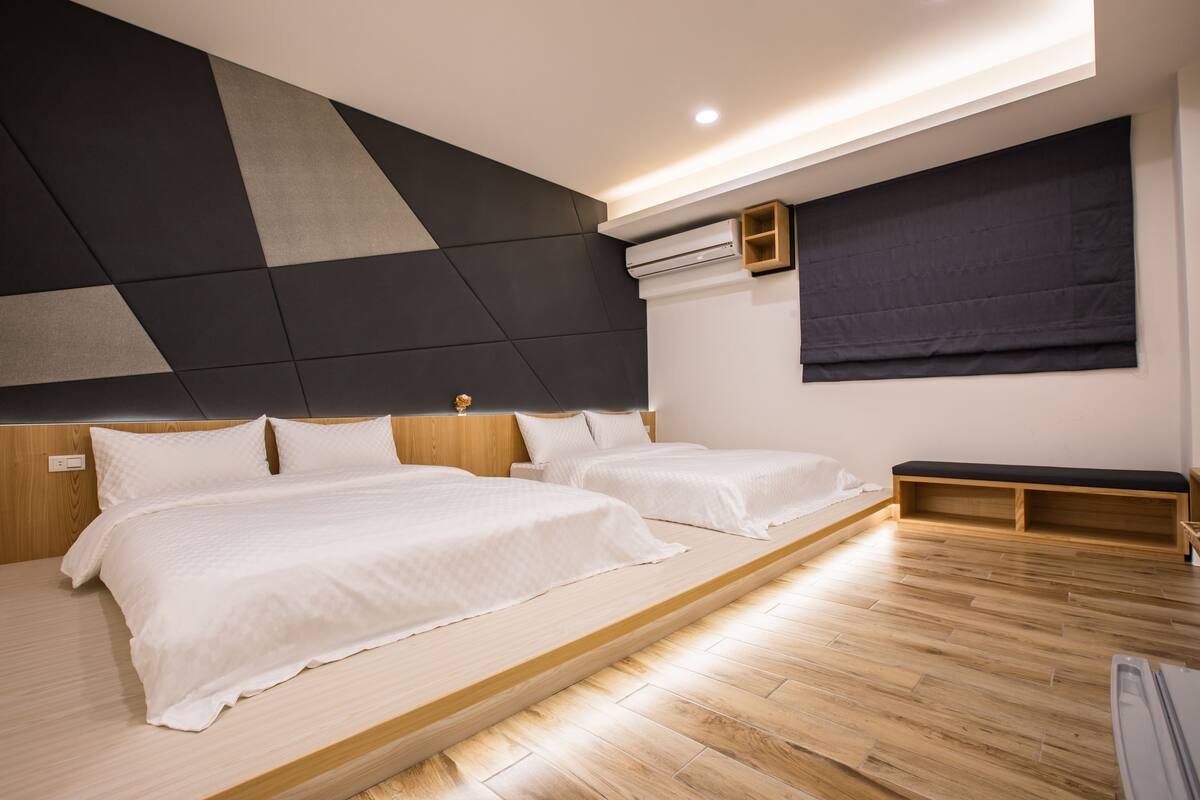 Un dormitorio moderno con dos camas, suelo de madera, diseño geométrico en la pared y almacenamiento integrado.