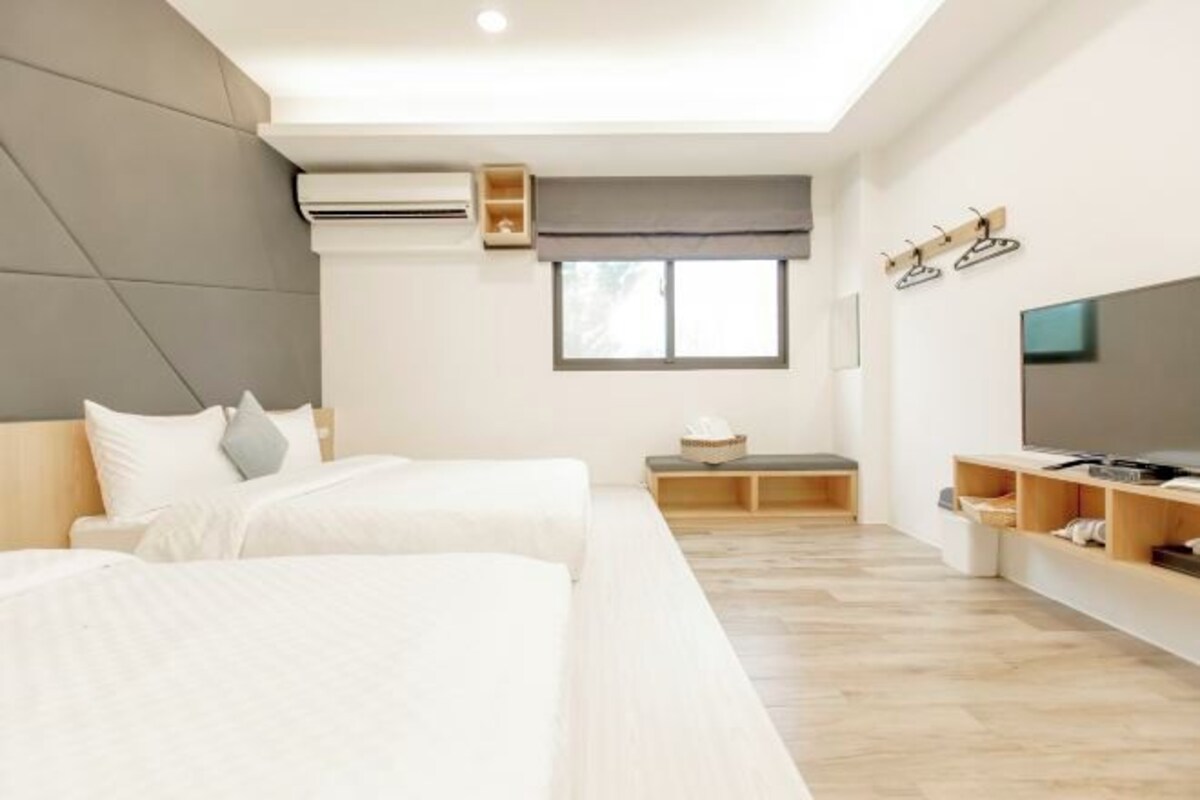 A modern hotel room with two beds, a TV, a wardrobe, and a window.